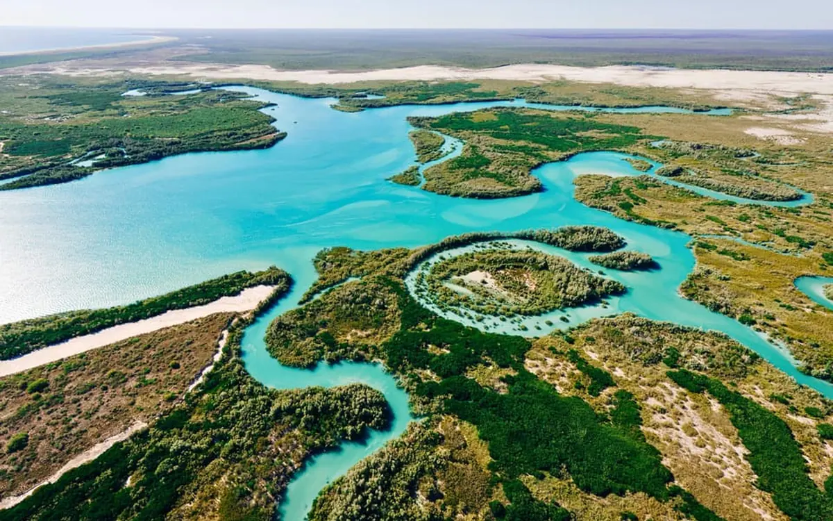 A helicopter over the turquoise water and red coastline near Broome